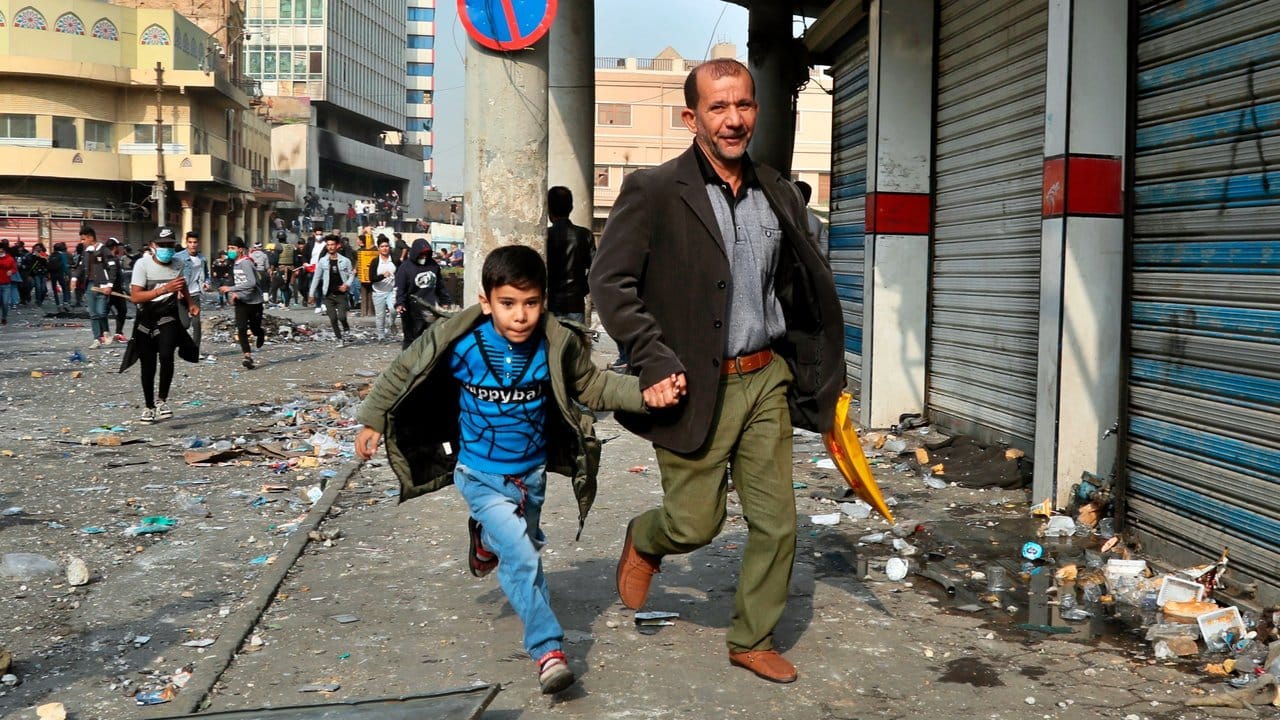 Ein Mann und sein Sohn flüchten vor Zusammenstößen zwischen irakischen Sicherheitskräften und regierungskritischen Demonstranten in Bagdad.