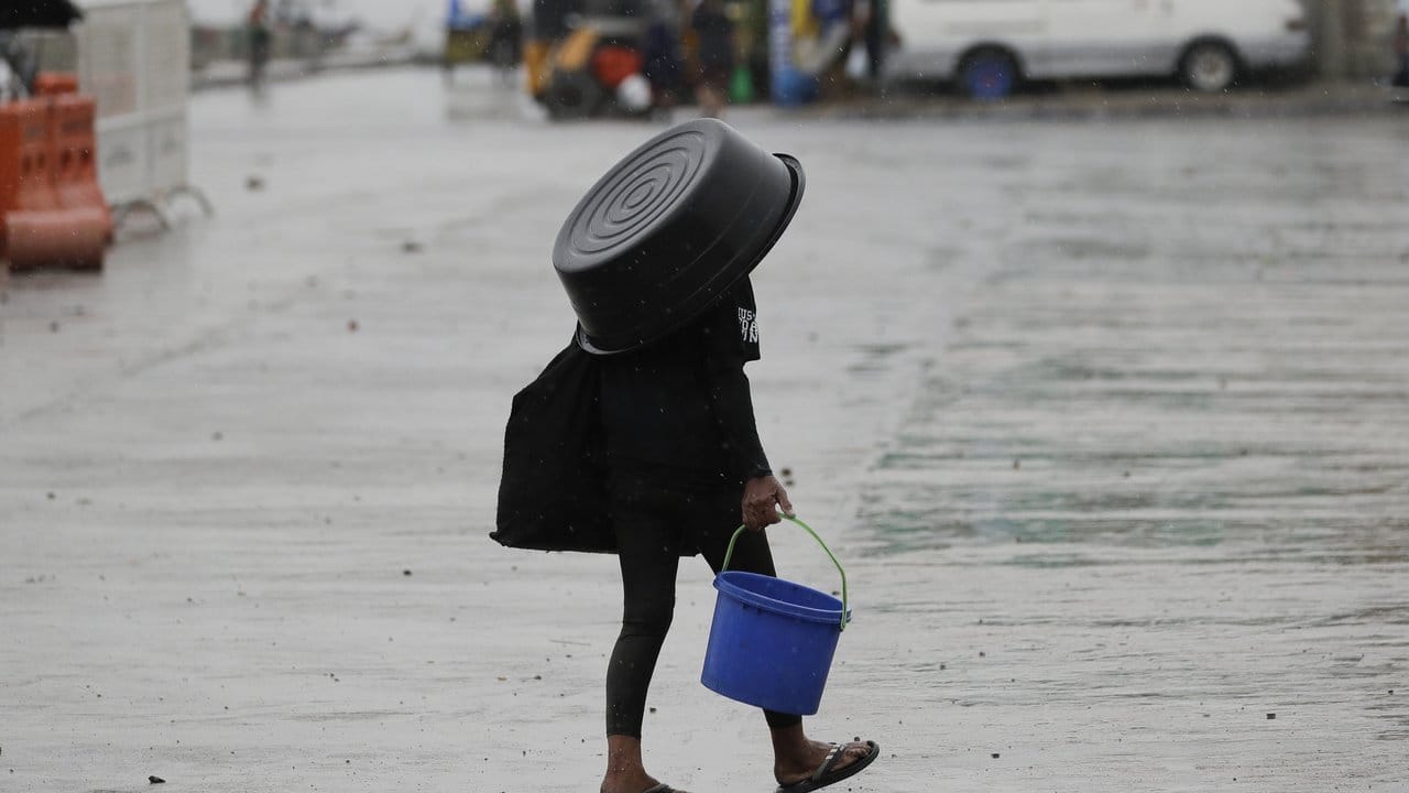 Eine Frau nutzt einen Plastikbehälter, um sich vor dem Regen in Manila zu schützen.