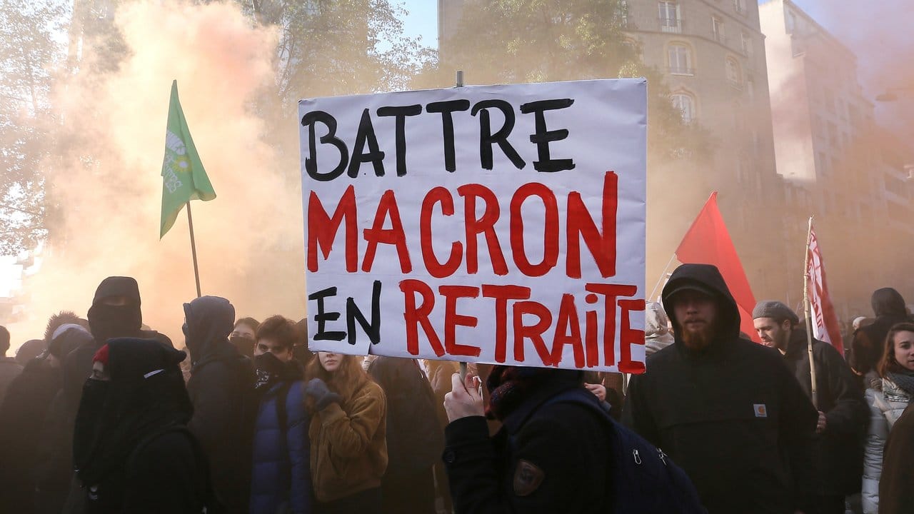 Demonstranten tragen ein Plakat mit der Aufschrift "Battre Macron en Retraite" (sinngemäß: "Macron zum Rücktritt zwingen").