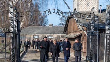 Bundeskanzlerin Angela Merkel und Polens Ministerpräsident Mateusz Morawiecki gehen im einstigen Vernichtungslager Auschwitz durch den Eingang mit der Aufschrift: "Arbeit Macht Frei".