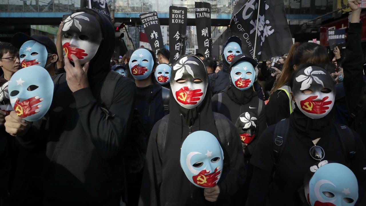 Demonstranten tragen Masken, auf denen eine rote Hand mit chinesischer Flagge den Mund zuhält.