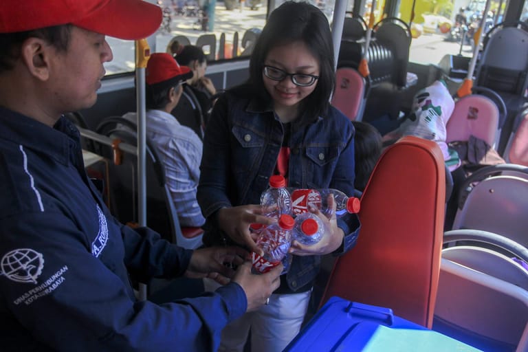 Eine Frau mit Plastikflaschen im Bus: In der indonesischen Stadt Surabaya können in bestimmten Bussen Plastikflaschen und -dosen gegen Fahrkarten getauscht werden. Fünf Flaschen gelten für ein zweistündiges Ticket.