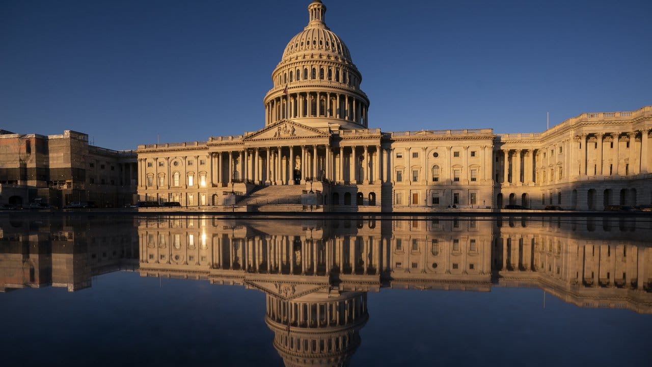 Das Kapitol der USA spiegelt sich in Wasser während des Sonnenaufgangs.