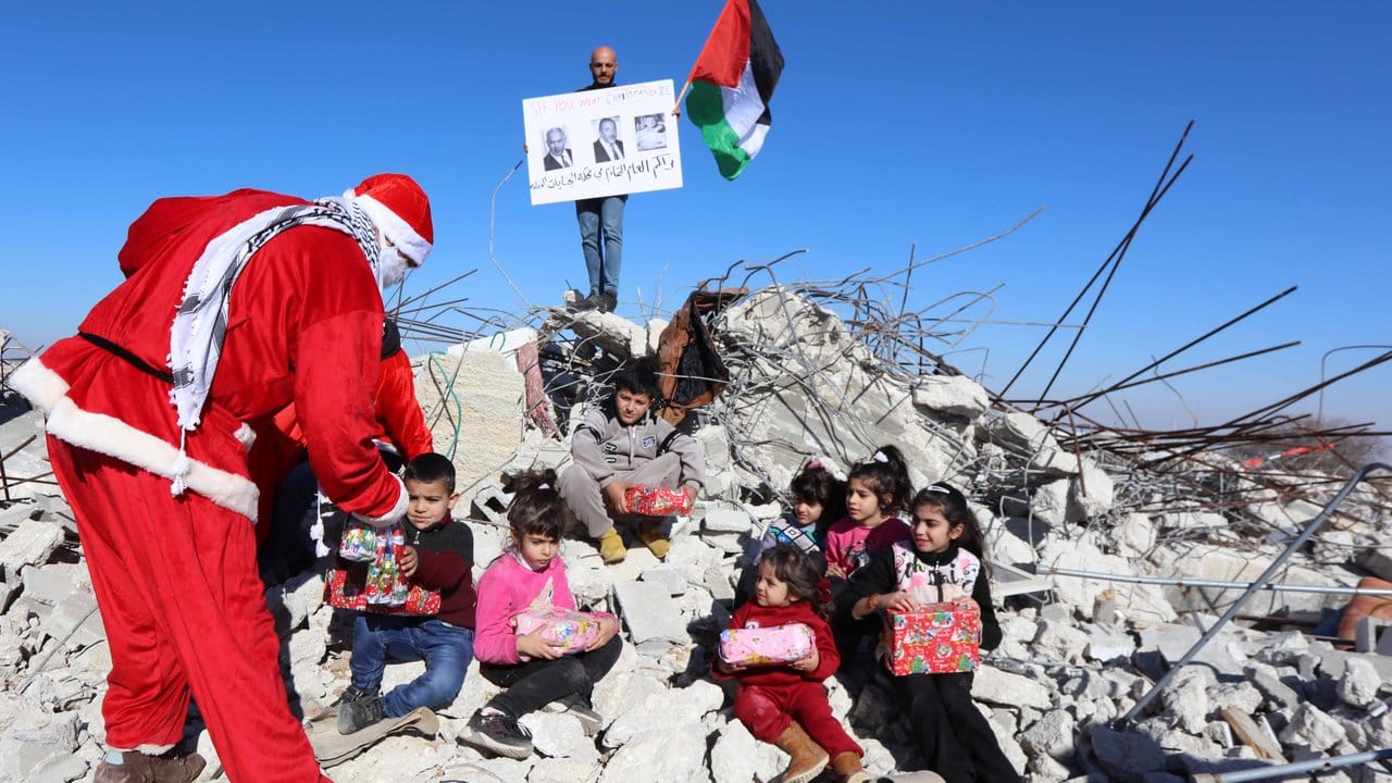 Ein Palästinenser im Weihnachtsmannkostüm verteilt Geschenke und Süßigkeiten an Kinder, die auf den Überresten zerstörter Häuser sitzen.