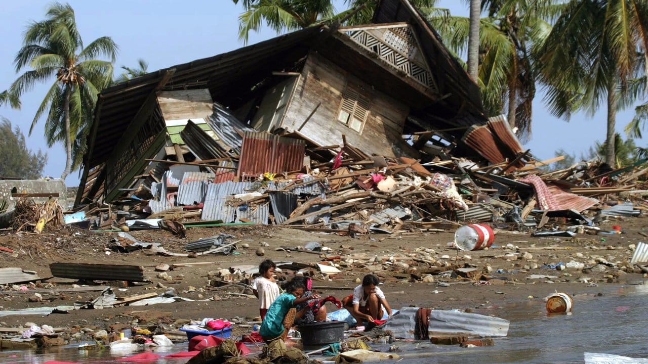 Frauen und Kinder, die den Tsunami in der Nähe von Banda Aceh überlebt haben, hocken vor einem zerstörten Haus an einer Wasserstelle.