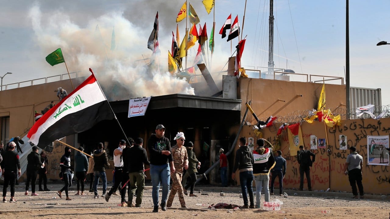 Demonstranten stehen mit Fahnen vor der US-Botschaft in Bagdad.
