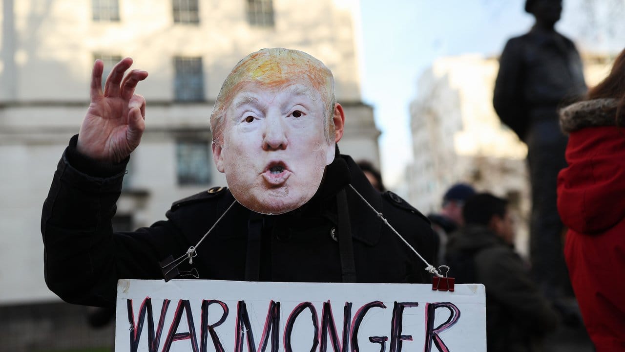 "Kriegstreiber" steht auf einem Schild, das ein Demonstrant mit Trump-Maske bei einem Protest in London hält.