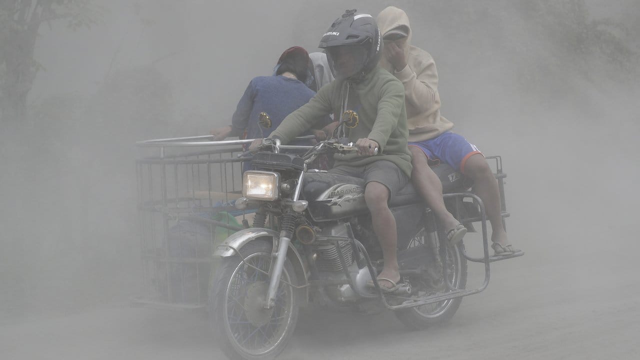 Eine Familie fährt in der Provinz Cavite auf einem Motorrad durch eine Aschewolke. Eine Familie fährt in der Provinz Cavite auf einem Motorrad durch eine Aschewolke.