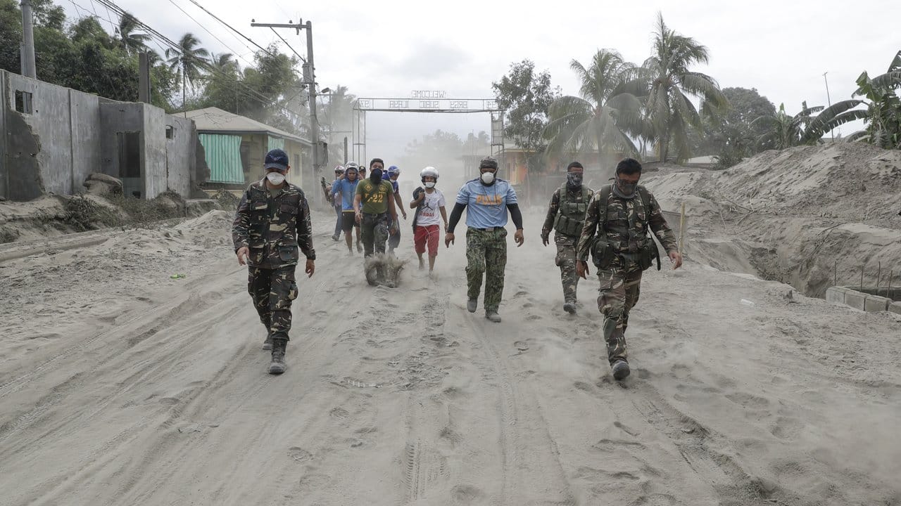 Philippinische Polizisten und Soldaten laufen auf einer mit Vulkanasche bedeckten Straße.