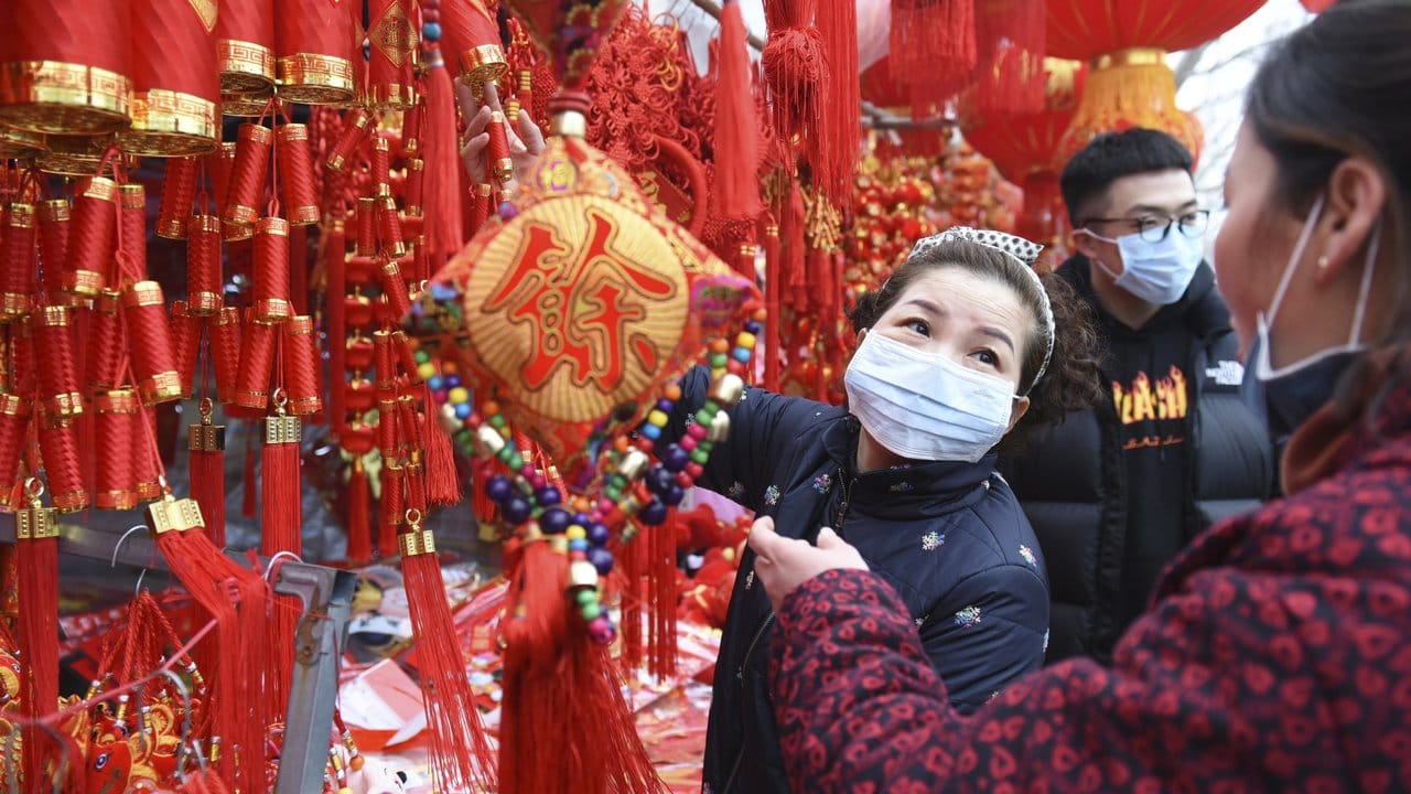 In der zentralchinesischen Provinz Anhui decken sich Menschen auf einem Markt mit Dekoration für das Neujahrsfest ein - und tragen Mundschutz.