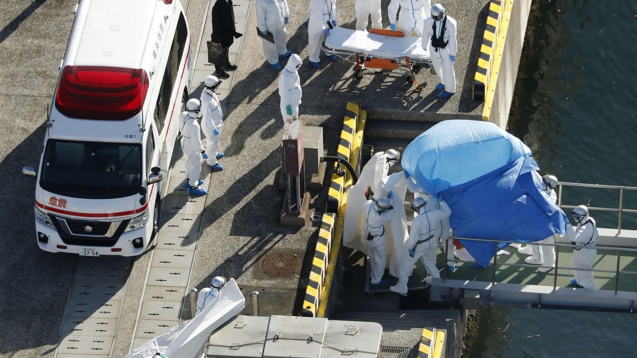 Medizinisches Personal in Schutzanzügen begleitet im Hafen von Yokohama einen Passagier, der auf dem Kreuzfahrtschiff "Diamond Princess" positiv auf das Coronavirus getestet wurde.