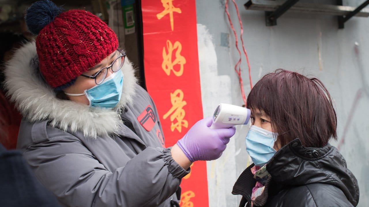 Eine Gemeindemitarbeiterin misst die Körpertemperatur einer Passantin in der Nähe der Kranichpagode in Wuhan.