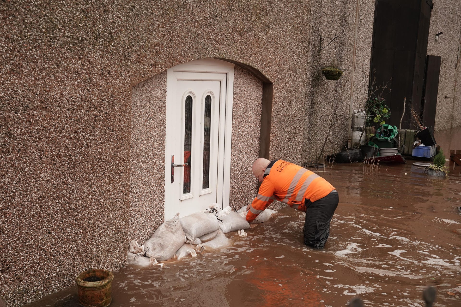 Ein Mann in Appleby-in-Westmorland sichert einen überfluteten Hauseingang mit Sandsäcken: Mehrere Veranstaltungen wurden wegen des Wetters abgesagt, darunter auch das Premier-League-Fußballspiel zwischen Manchester City und West Ham.
