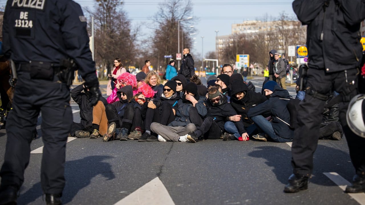 Gegendemonstranten sitzen aus Protest gegen den Neonazi-Aufmarsch auf einer Straße.