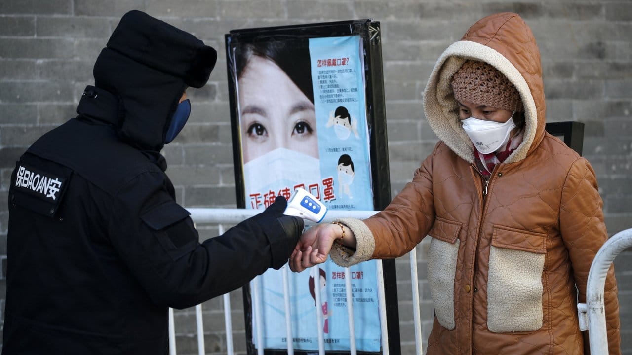 Momentaner Alltag in Peking: Ein Sicherheitsmann misst die Temperatur bei einer Frau.