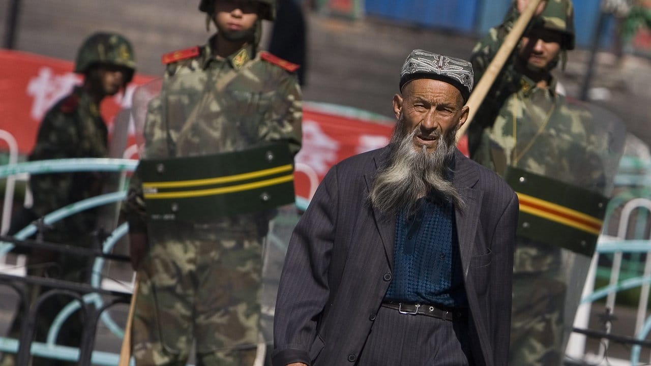 Ein Angehöriger der uigurischen Minderheit in der Unruheregion Xinjiang geht an chinesischen Sicherheitskräften vorbei.