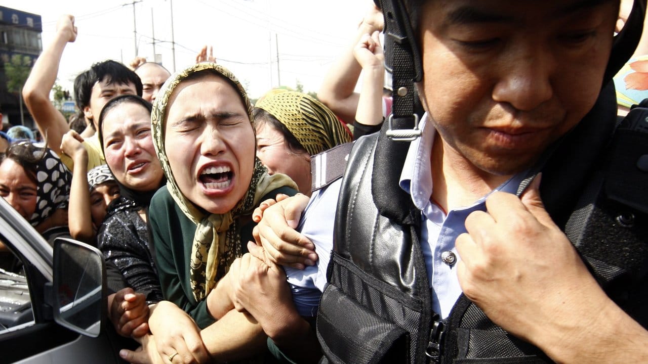 Uiguren rangeln bei einer Demonstration mit einem Polizisten.