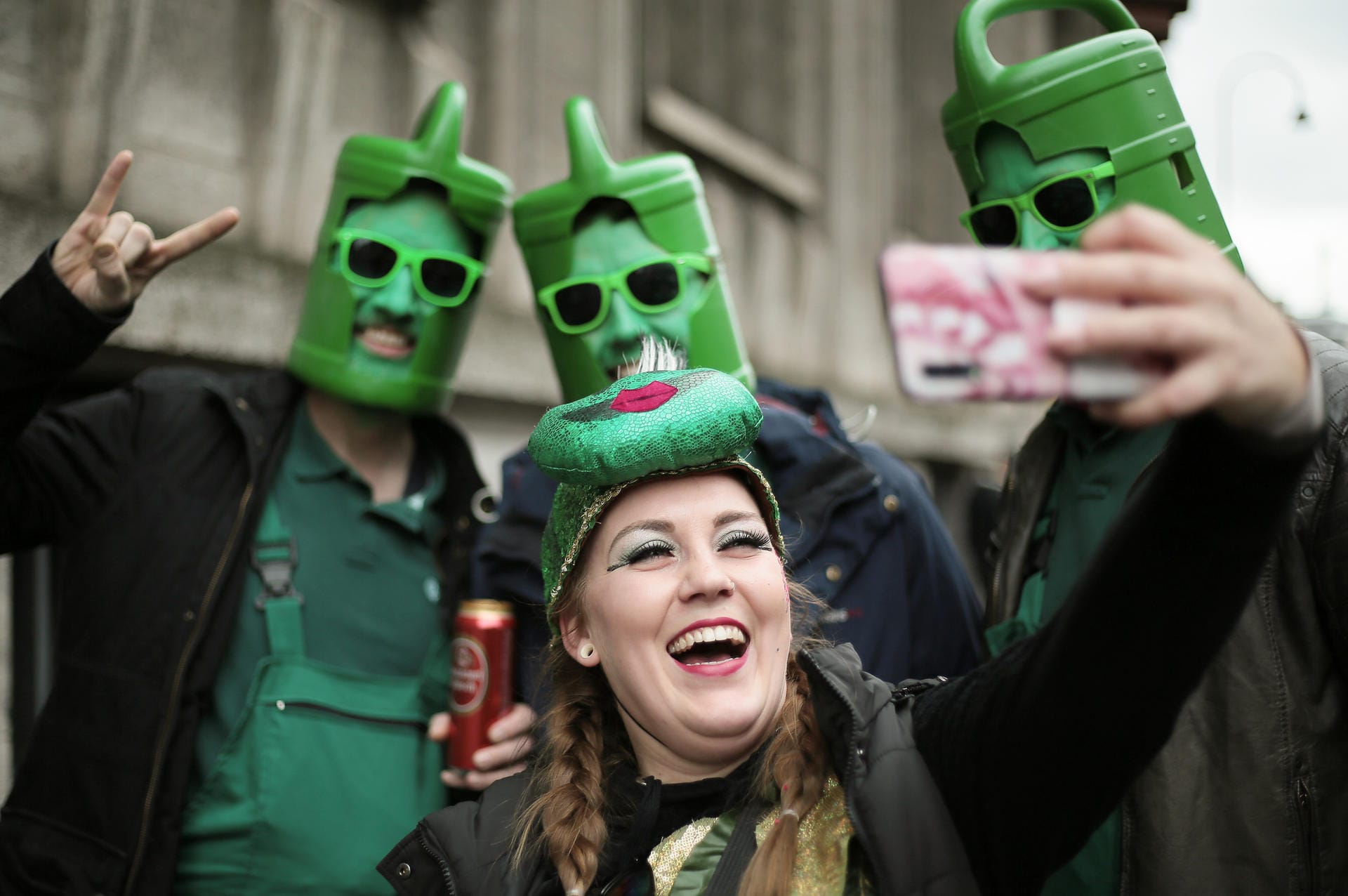 Eine Karnevalistin fotografiert sich mit Männern, die Gießkannen auf dem Kopf tragen.