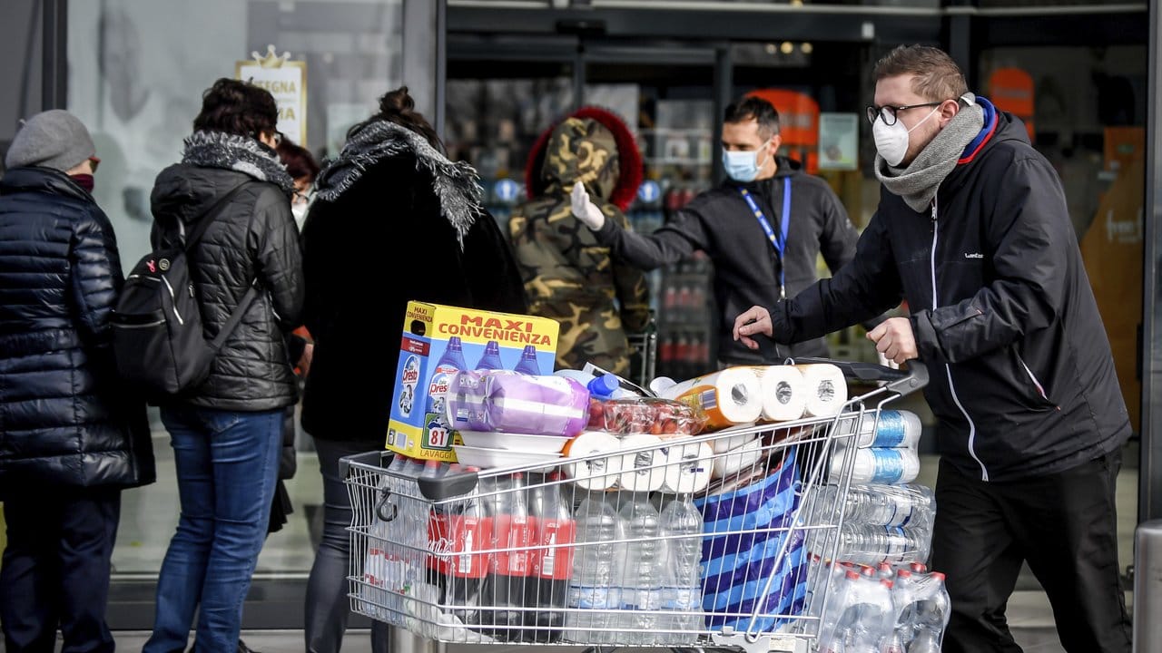 Menschen stehen mit Atemschutzmasken vor einem Supermarkt in der Lombardei.