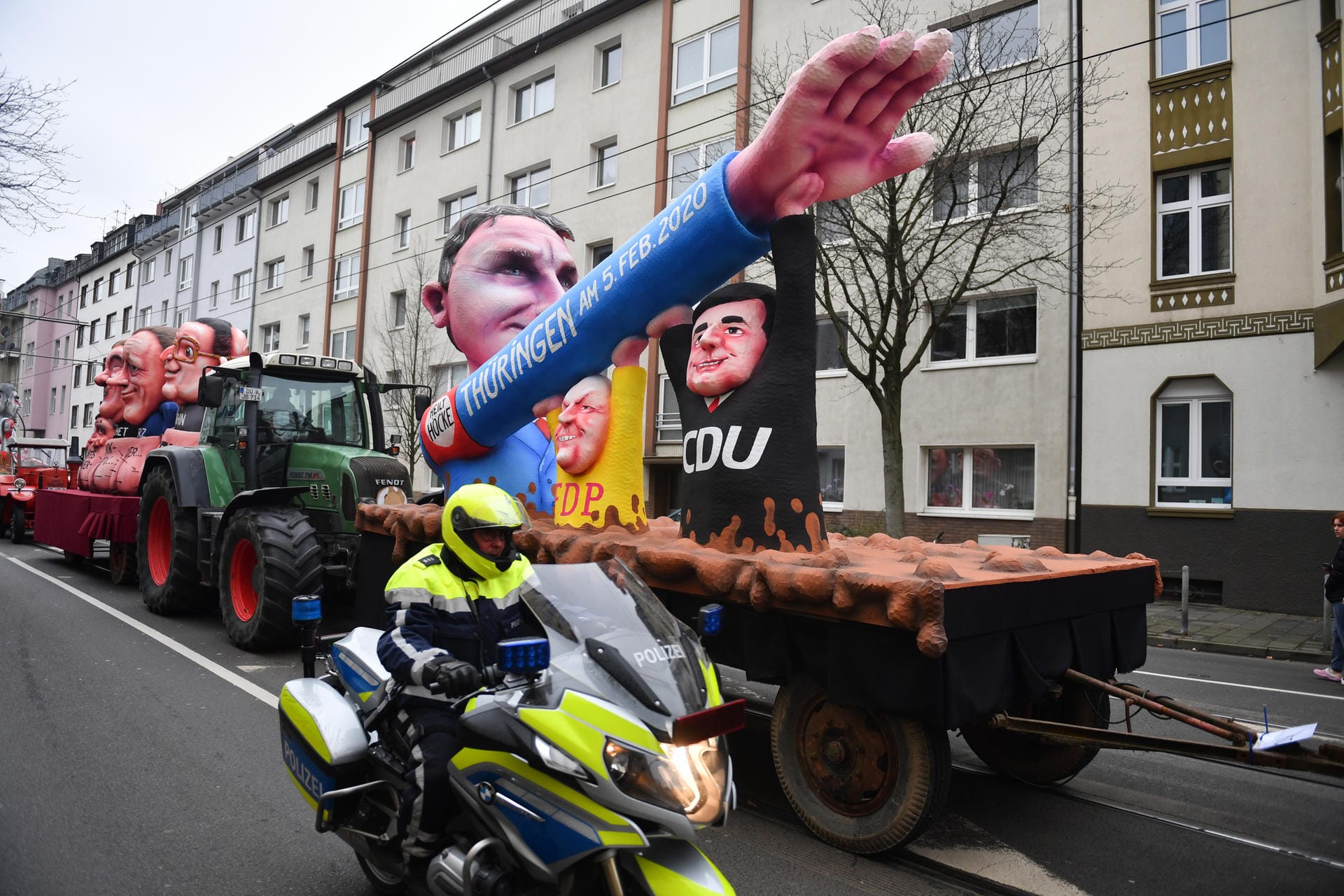 Ein Polizist auf einem Motorrad fährt am Motivwagen "Thüringen und Björn Höcke" vorbei: Mit den Rosenmontagszügen erreicht der rheinische Straßenkarneval seinen Höhepunkt.