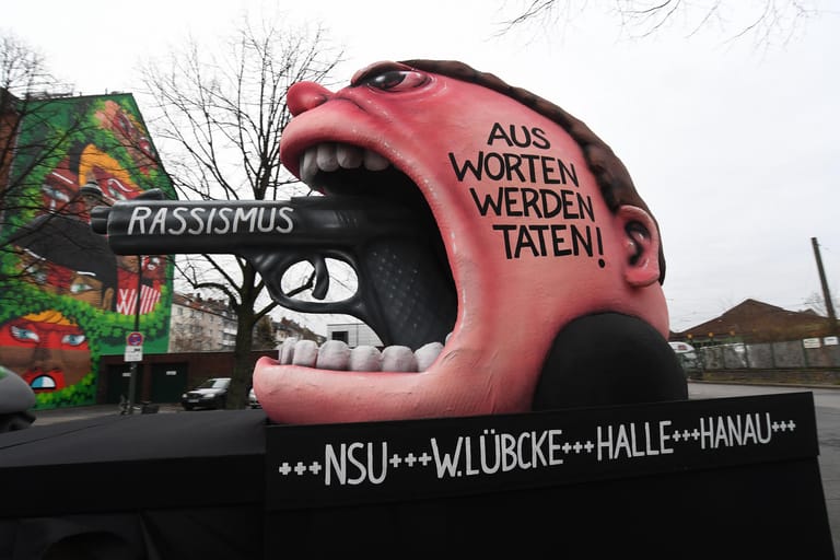 Der Motivwagen "Rassismus – Aus Worten werden Taten! +++ NSU +++ W. Lübcke +++ Halle +++ Hanau" steht vor dem Rosenmontagszug auf der Straße: Mit den Rosenmontagszügen erreicht der rheinische Straßenkarneval seinen Höhepunkt.