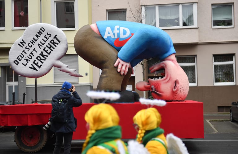 Jecken laufen am Motivwagen "AfD" vor dem Rosenmontagszug: Mit den Rosenmontagszügen erreicht der rheinische Straßenkarneval seinen Höhepunkt.
