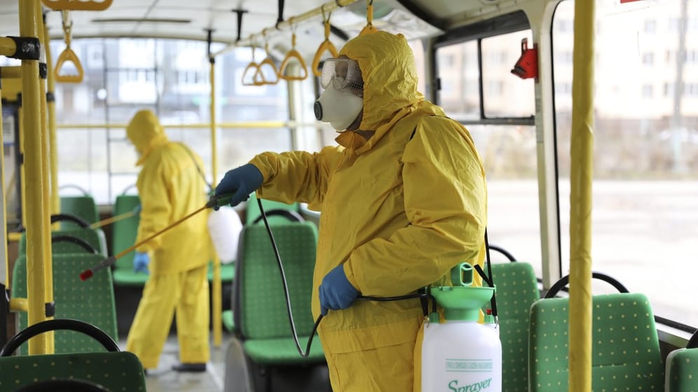 Mitarbeiter in Schutzausrüstung versprühen im ukrainischen Lwiw Desinfektionsmittel in einem Bus.
