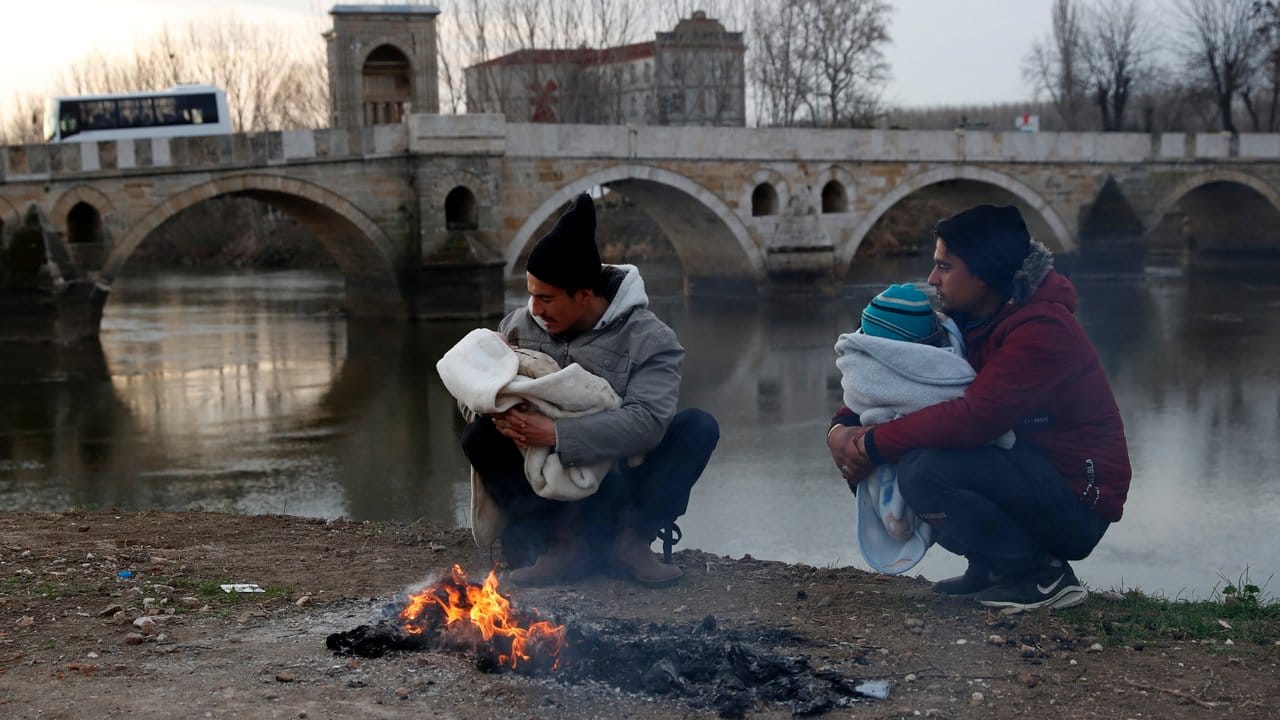 Migranten halten ihre Babys in den Armen neben einem Lagerfeuer am Ufer des Flusses nahe der türkisch-griechischen Grenze.