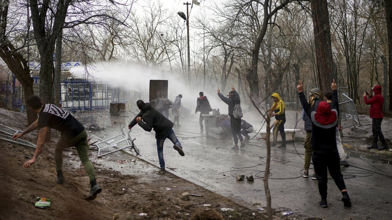 Migranten werfen Steine, die griechische Polizei setzt einen Wasserwerfer ein.