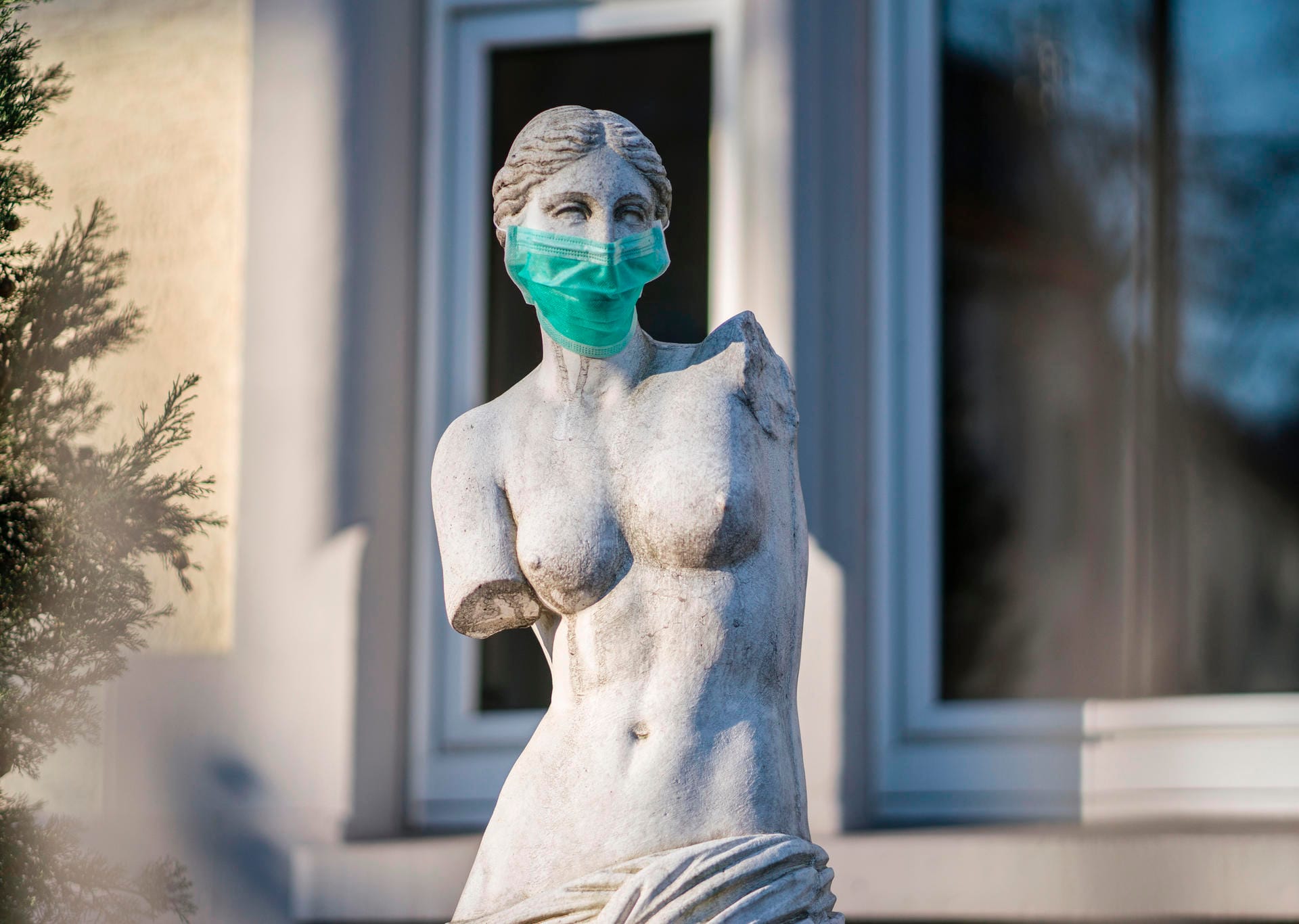 Eine Replik einer berühmten antiken Statue, der Venus von Milo, steht mit einem Mundschutz in einem Frankfurter Vorgarten.