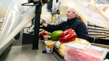 Langballig: Eine Kassiererin von Edeka sitzt unter einer Plastikfolie zum Schutz vor dem Coronavirus.