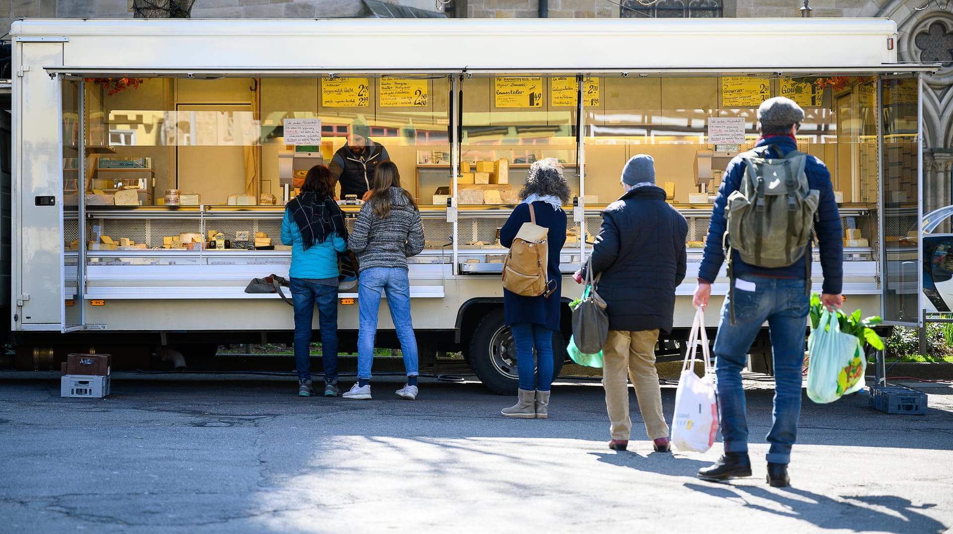 Kunden stehen mit Abstand auf dem Markt vor einem Stand an. Um die Ausbreitung des Coronavirus zu verlangsamen ist das öffentliche Leben weitgehend zurück gefahren.