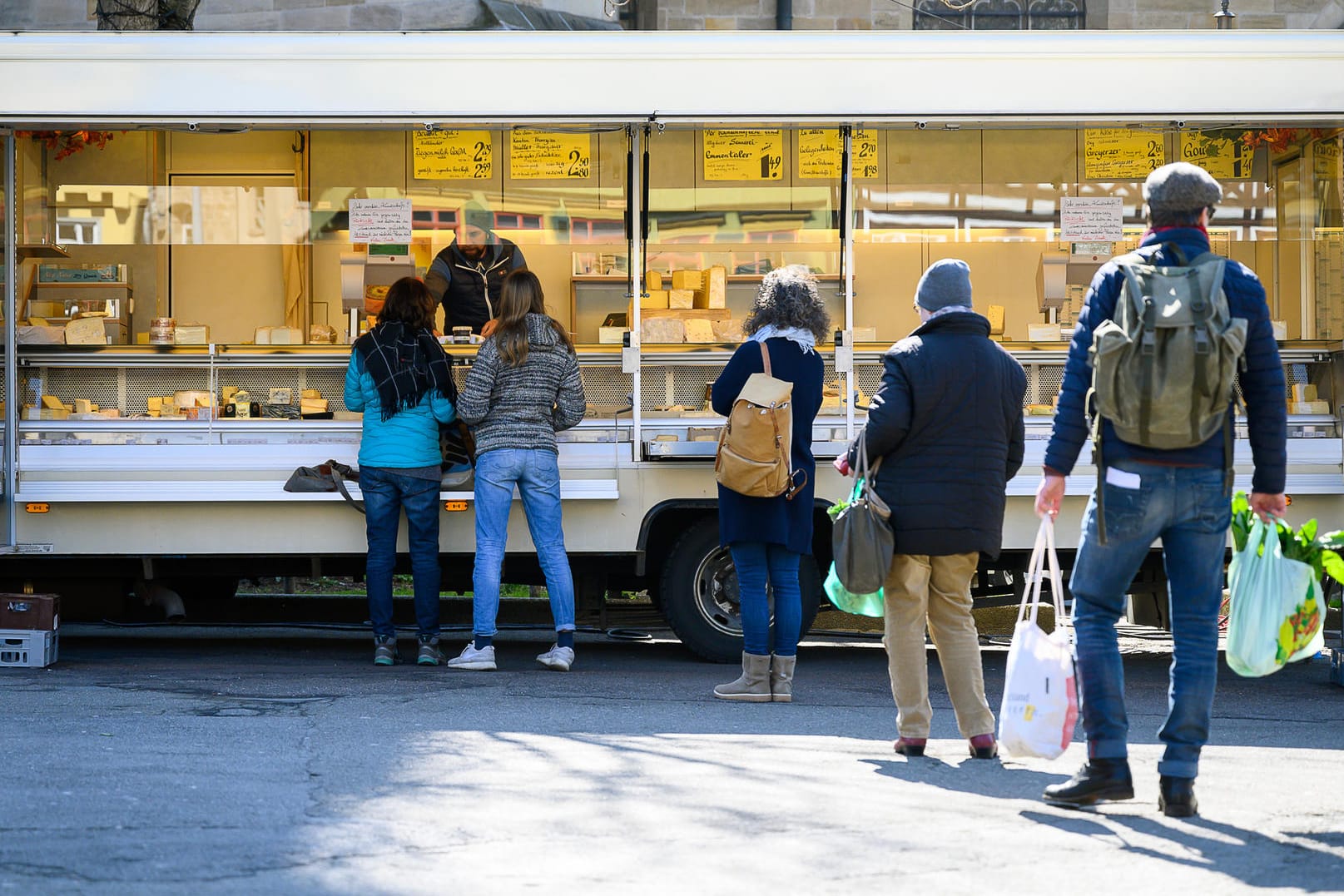 Kunden stehen mit Abstand auf dem Markt vor einem Stand an. Um die Ausbreitung des Coronavirus zu verlangsamen ist das öffentliche Leben weitgehend zurück gefahren.