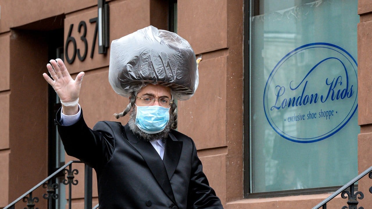 Ein chassidischer Jude in Brooklyn trägt einen Mundschutz, Handschuhe und einen Schutz über seinem Schtreimel, der traditionellen Kopfbedekung.