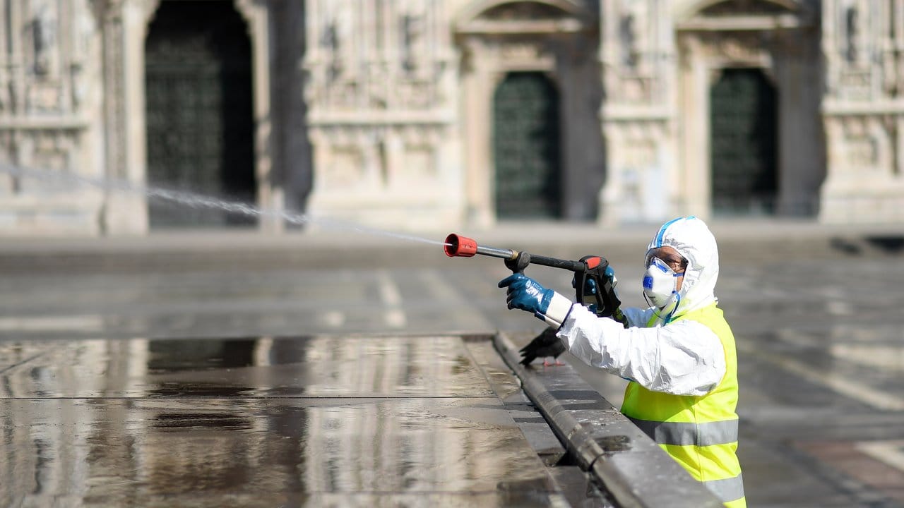 Ein Arbeiter in Schutzanzug reinigt den Piazza del Duomo in Mailand. Ein Arbeiter in Schutzanzug reinigt den Piazza del Duomo in Mailand.