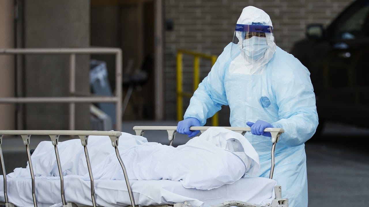 Ein Mitarbeiter in Schutzkleidung bringt eine Leiche zu einem Kühlanhänger, der als behelfsmäßige Leichenhalle im Wyckoff Heights Medical Center in New York dient.