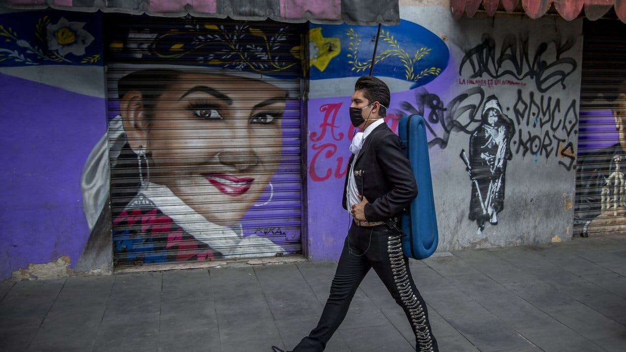 Ein Mariachi mit Mundschutz geht vor einem Wandgemälde von Aida Cuevas, einer Ikone der mexikanischen Musik.