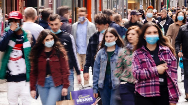 Menschen mit Maske in der Fußgängerzone, die beim Einkaufen und Shoppen während der Corona-Maßnahmen Pflicht ist.