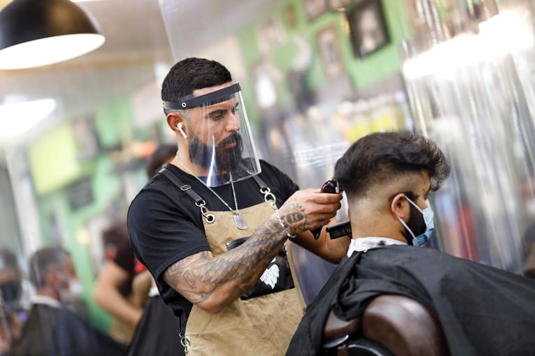 Friseure wie dieser Kölner Barber müssen sich und ihre Kunden mit Masken schützen.