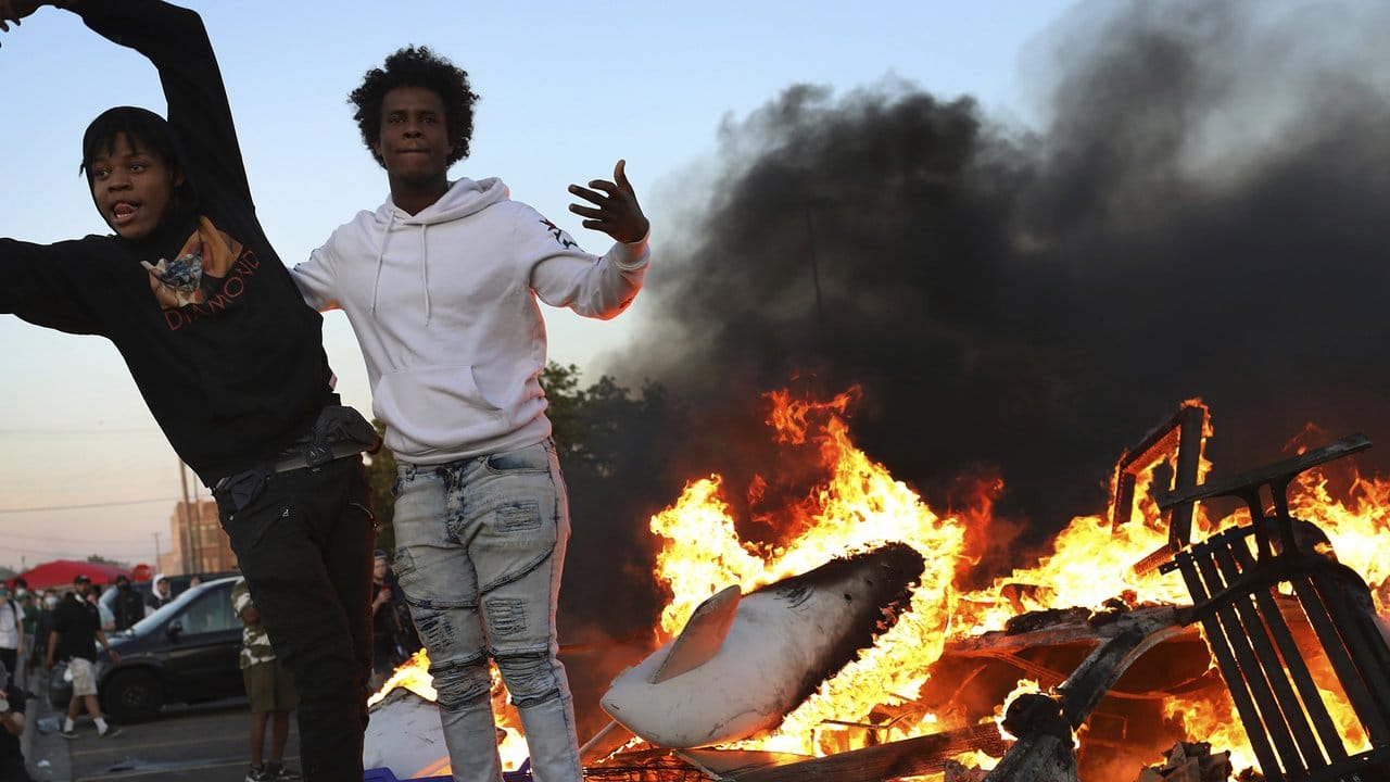 Demonstranten stehen auf einem brennenden Auto.