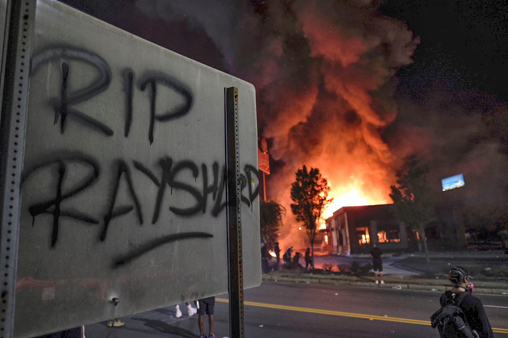 "RIP Rayshard" steht auf einem Schild, während im Hintergrund ein "Wendy's"-Restaurant brennt.