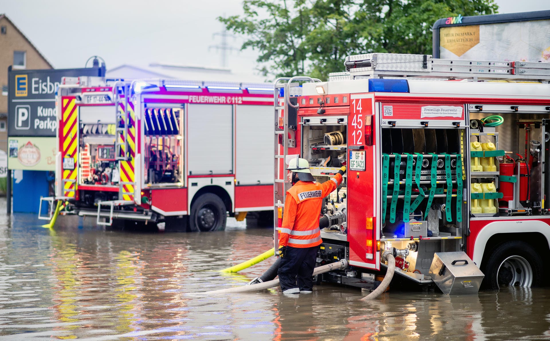 Niedersachsen: Zwei Einsatzfahrzeuge der Feuerwehr steht auf dem überschwemmten Parkplatz eines Supermarktes im Landkreis Gifhorn, der durch Starkregen überflutet wurde und abgepumpt werden muss.