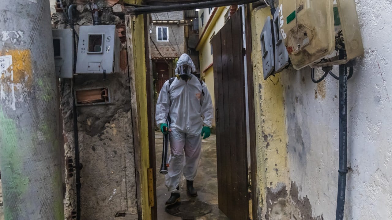 Ein Mann mit Schutzkleidung und einem Gerät zur Straßendesinfektion in einem Armenviertel von Rio de Janeiro. Ein Mann mit Schutzkleidung und einem Gerät zur Straßendesinfektion in einem Armenviertel von Rio de Janeiro.