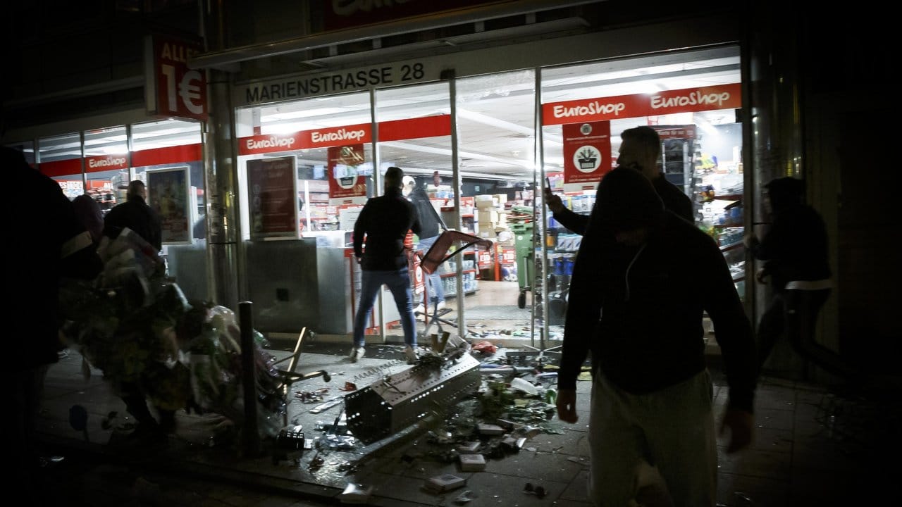 Menschen stehen in der Krawallnacht vor einem geplünderten Geschäft in der Stuttgarter Innenstadt. Menschen stehen in der Krawallnacht vor einem geplünderten Geschäft in der Stuttgarter Innenstadt.