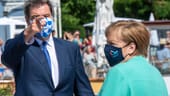 Willkommen in Bayern: Söder – mit weiß-blau-karrierter Maske – und Kanzlerin Merkel – ebenfalls mit Maske – an der Schiffsanlegestelle Prien vor der Überfahrt mit einem Schiff auf die Insel Herrenchiemsee.