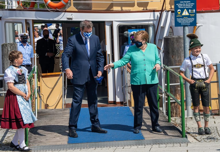 Aufstellung für die Fotografen: Zwei Kinder in Trachten stehen neben Merkel und Söder am Bootsanleger in Prien.