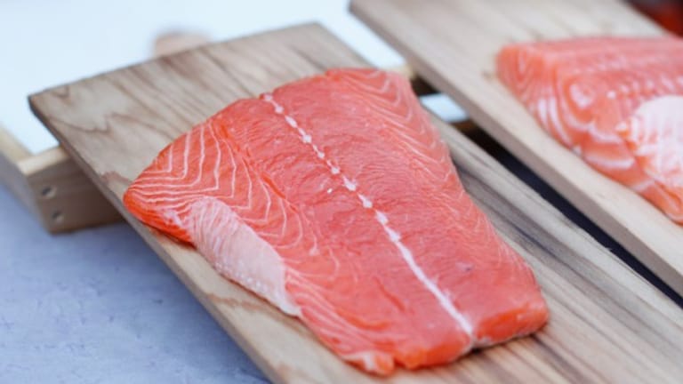Waschen Sie den Lachs und tupfen ihn dann mit einem Küchentuch etwas trocken. Pfeffern und salzen Sie den Fisch dann und legen Sie ihn auf die Holzplanken.
