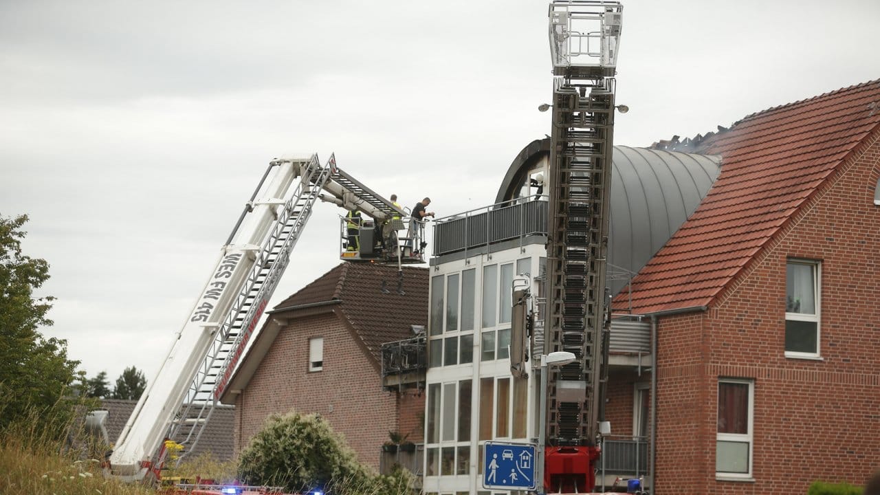 Feuerwehrleute nähern sich dem beschädigten Wohnhaus mit einer Drehleiter.