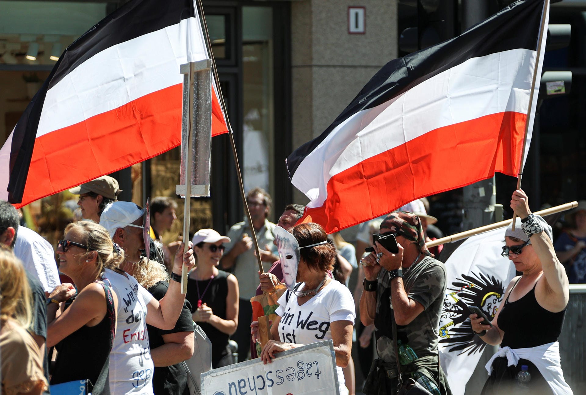 Mehrere Demonstranten sind mit Abwandlungen der Reichkriegsflagge sowie dem Wappen Preußens unterwegs. Rechtspopulisten sehen in ihnen Symbole eines angeblich verloren gegangenen unabhängigen und starken Deutschlands.