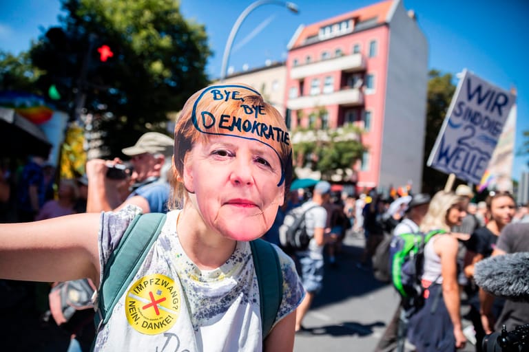 Eine Demonstrantin trägt das Konterfei Angela Merkels als Maske. Die Aussage, "Byebye Demokratie" wurde der Bundeskanzlerin dabei in den Mund gelegt.